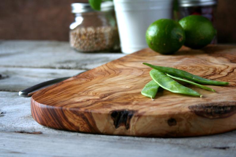 Rustic olive wood cutting board with rich grain patterns and natural edge on weathered white wood surface with fresh limes