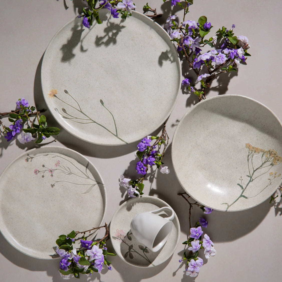 Handmade ceramic dinnerware set in speckled white glaze with delicate pressed botanical impressions and purple flowers