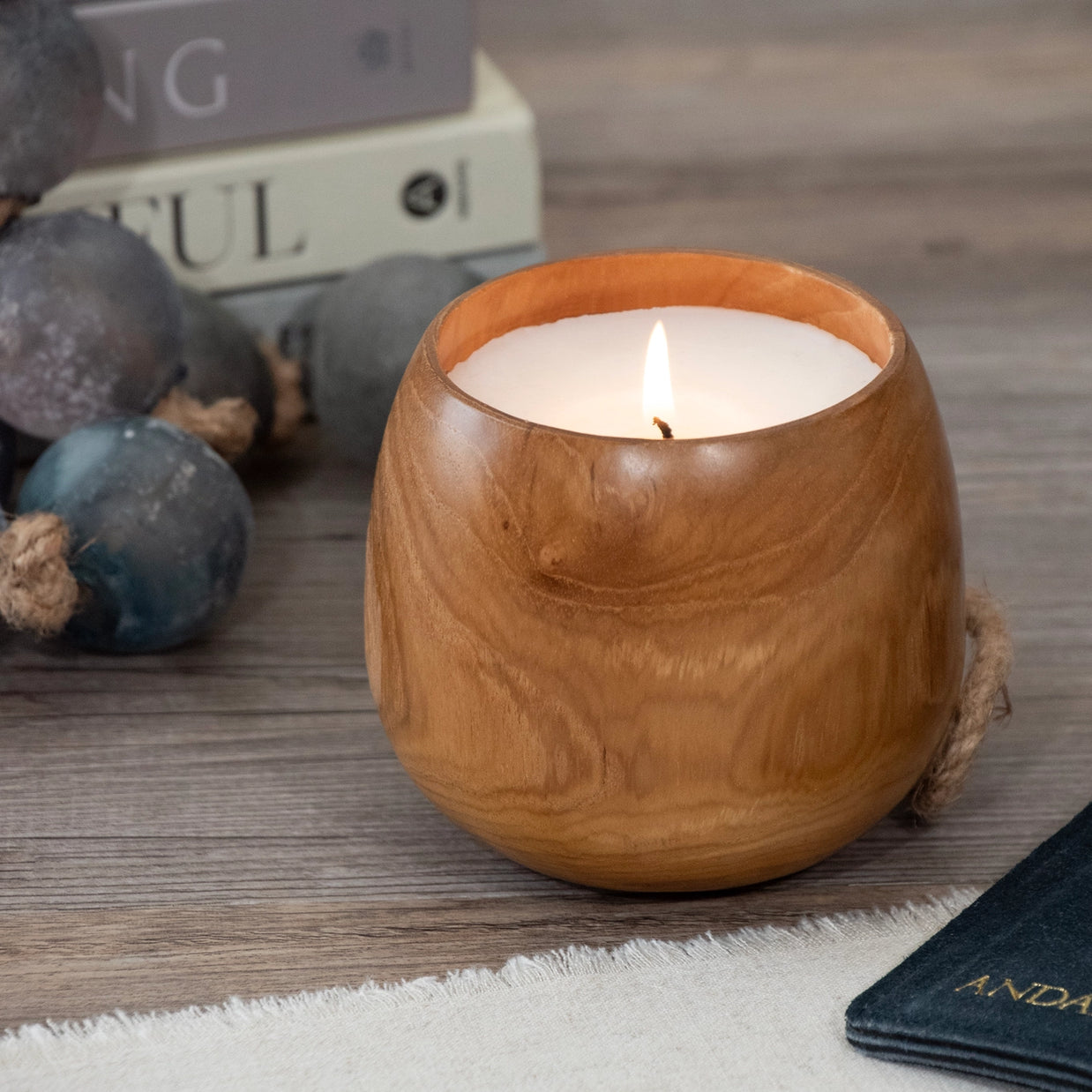 Rounded wooden bowl candle with white wax and lit wick, natural wood grain visible in warm honey brown tones