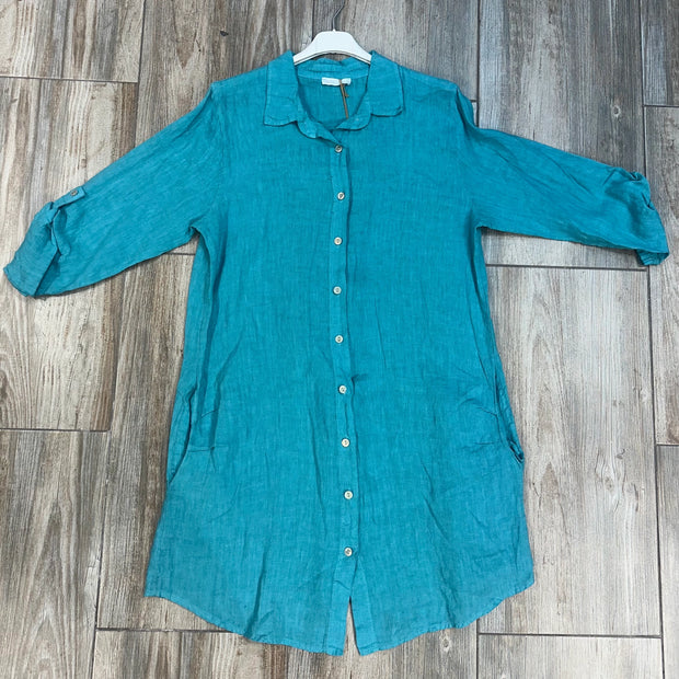 Turquoise linen button-down shirt with rolled three-quarter sleeves and collar hanging on white hanger against weathered wood floor