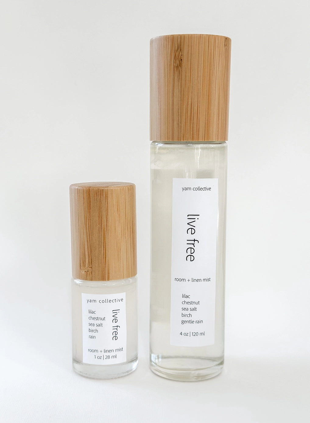 Two clear glass room spray bottles with bamboo wood caps, labeled live free with lilac and chestnut scent notes