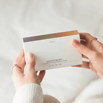 Hands holding white minimalist business card labeled Signature Kit with ombre copper to gray stripe accent on top edge