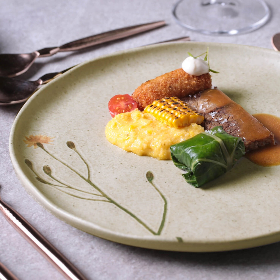 Plated gourmet dish on speckled sage green ceramic plate with braised meat, polenta, charred corn, and fried croquette