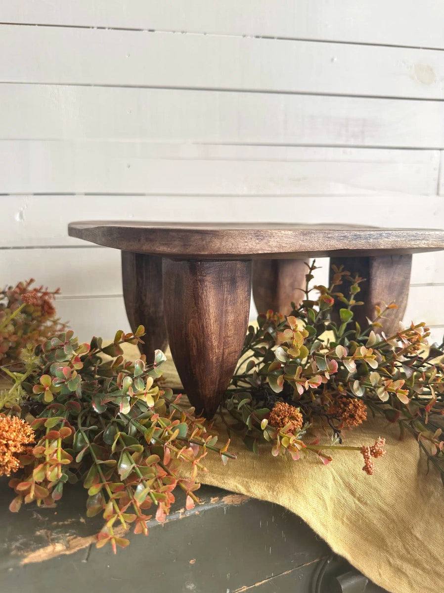 Rustic wooden pedestal cake stand with dark walnut finish and fluted base surrounded by autumn eucalyptus stems