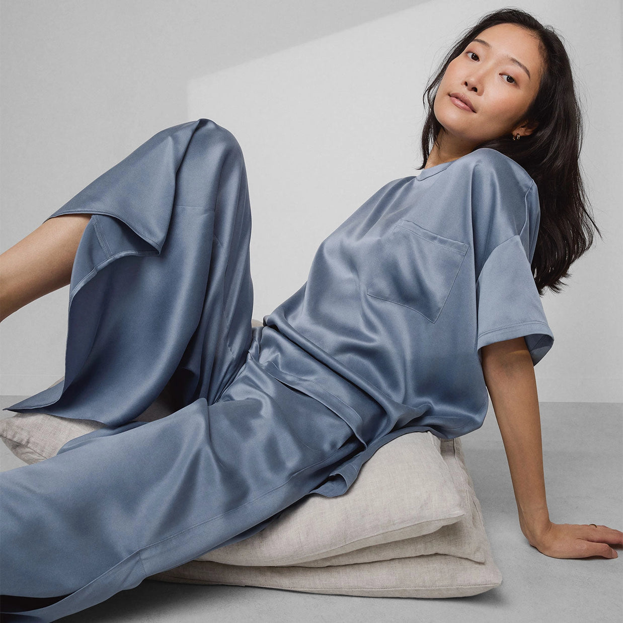 Dusty blue silk pajama set with short-sleeve pocket top and wide-leg pants with subtle sheen on neutral background