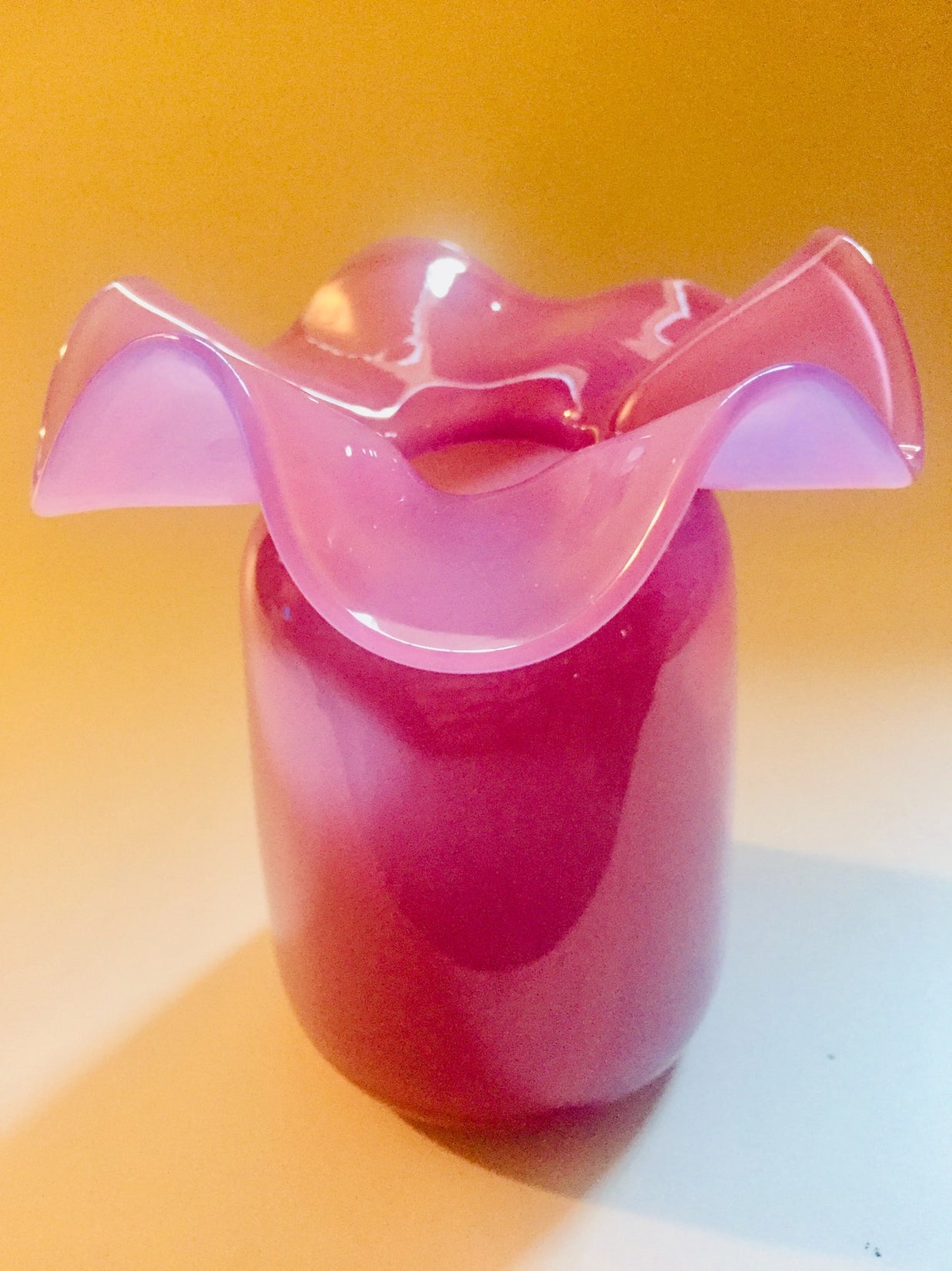 Pink frosted glass vase with ruffled scalloped rim and cranberry red cylindrical base on yellow background