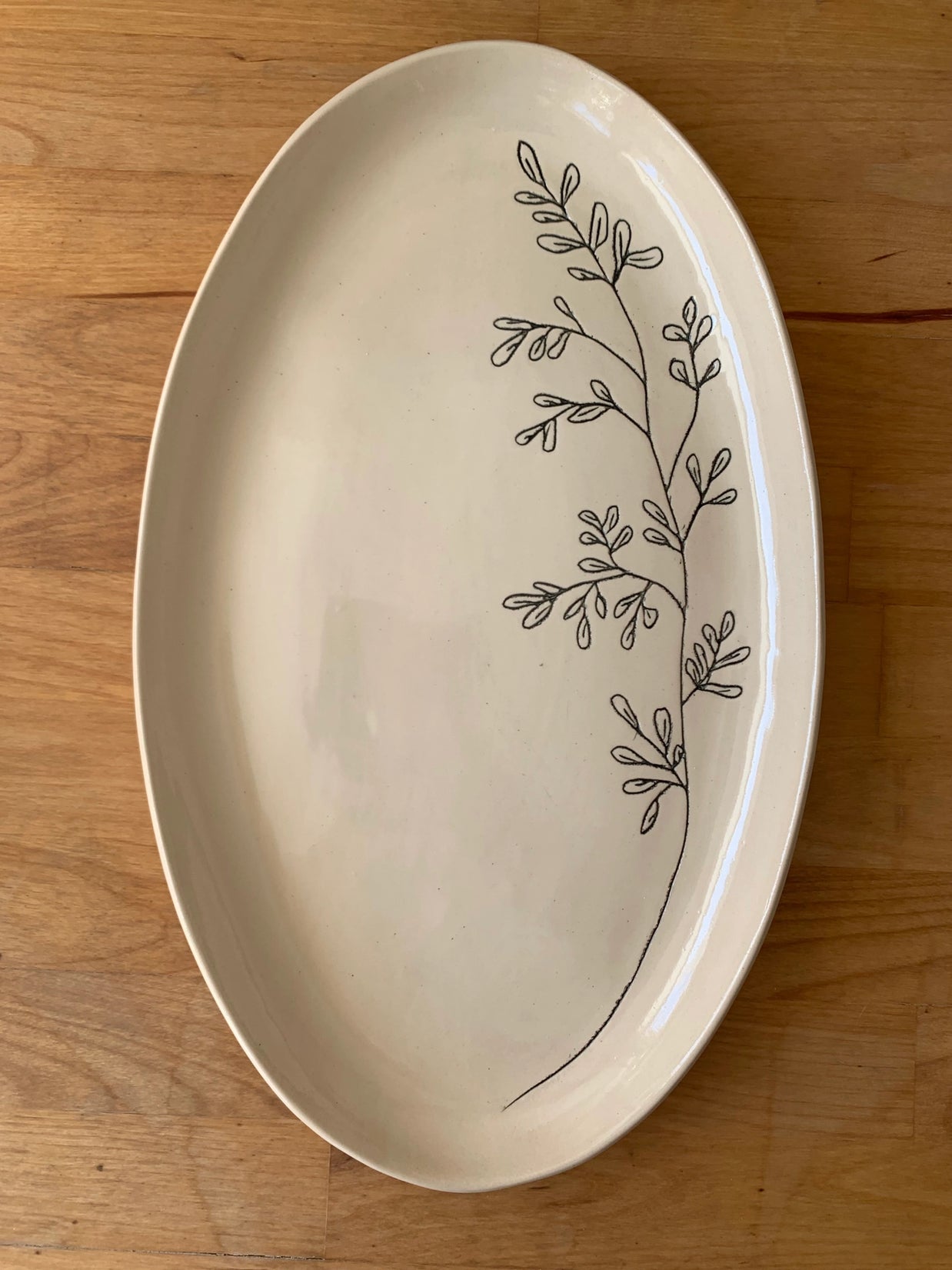 Cream oval ceramic platter with hand-drawn black botanical branch design featuring delicate leaves on glossy finish