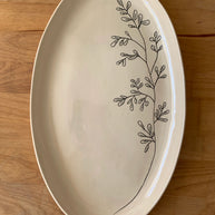 Cream oval ceramic platter with hand-drawn black botanical branch design featuring delicate leaves on glossy finish