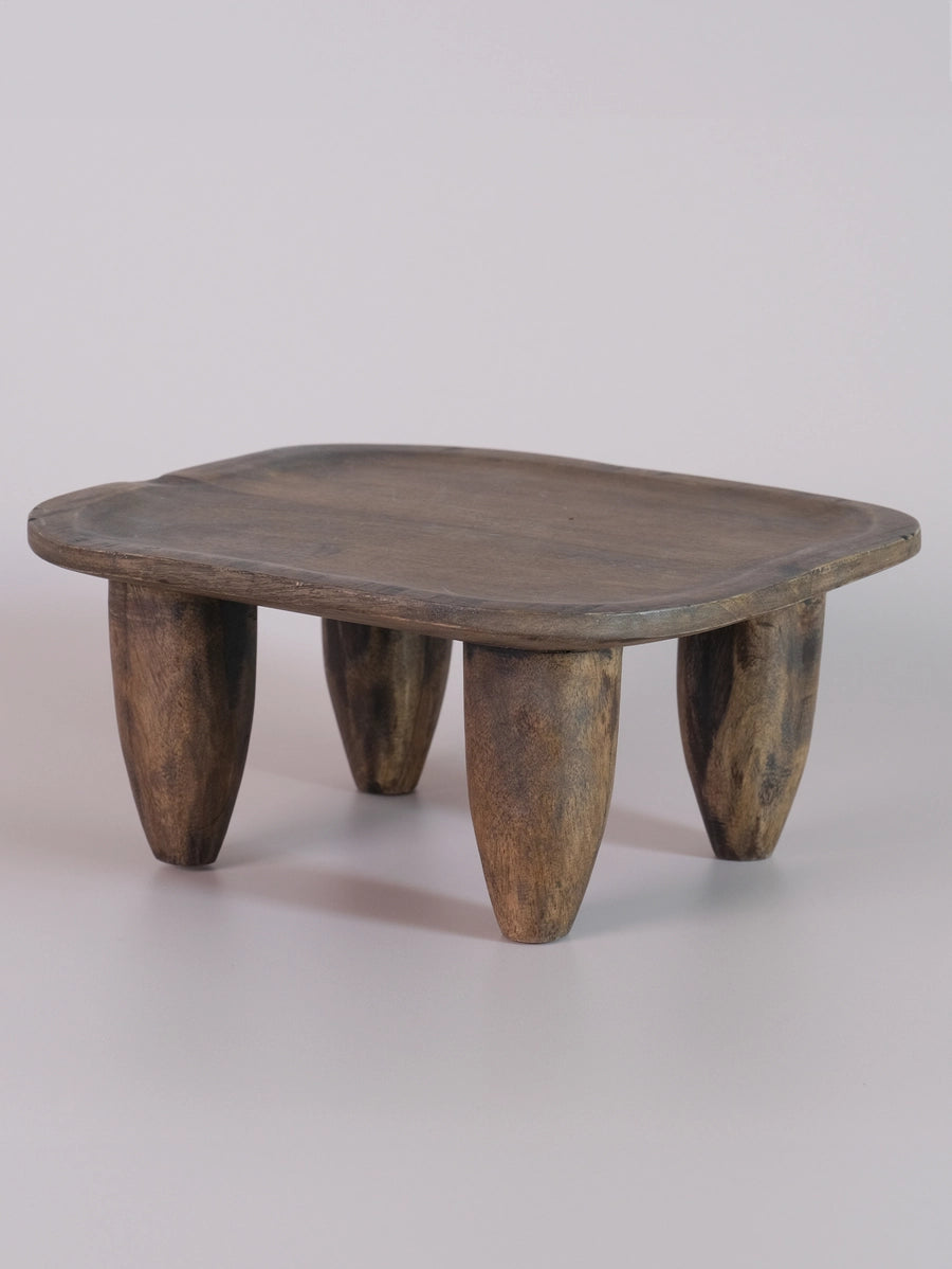 Hand-carved wooden stool with weathered gray-brown finish, organic rounded square top, and four tapered conical legs