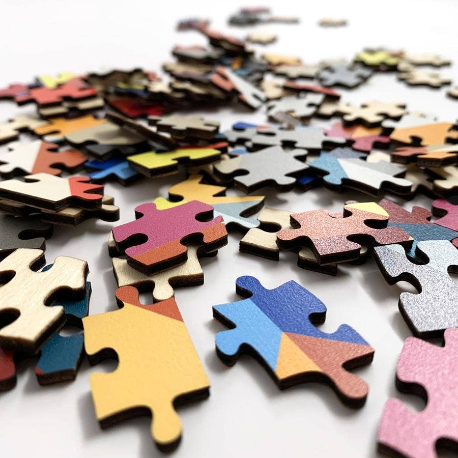 Scattered wooden jigsaw puzzle pieces in vibrant colors including pink, yellow, blue, coral, and cream on white surface