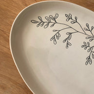 Cream ceramic plate with hand-drawn black botanical branch design featuring delicate leaves on natural wood surface