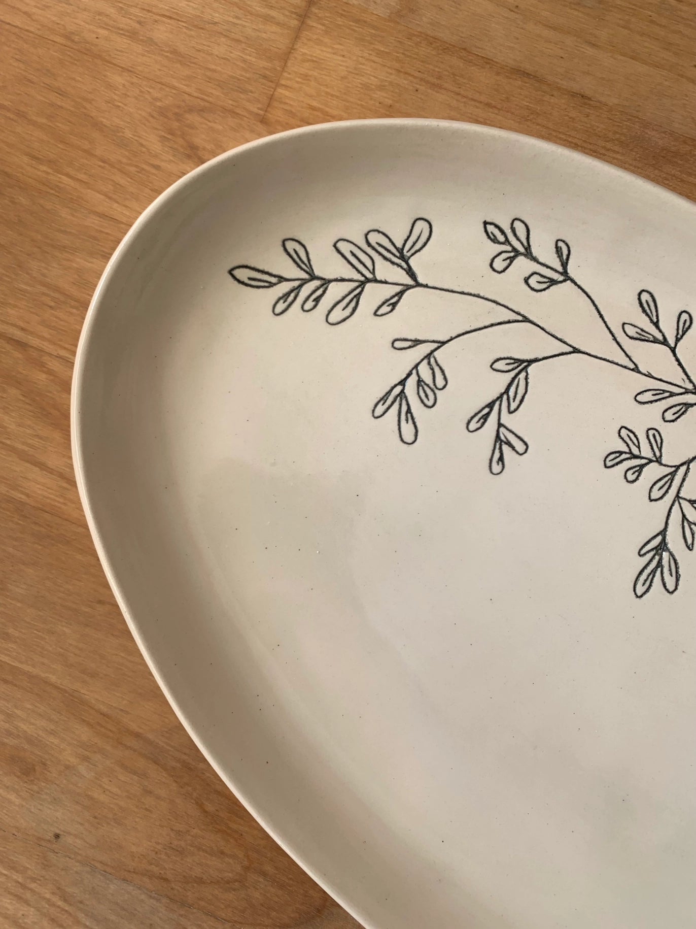 Cream ceramic plate with hand-drawn black botanical branch design featuring delicate leaves on natural wood surface