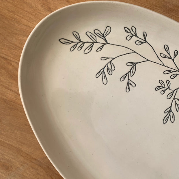 Cream ceramic plate with hand-drawn black botanical branch design featuring delicate leaves on natural wood surface