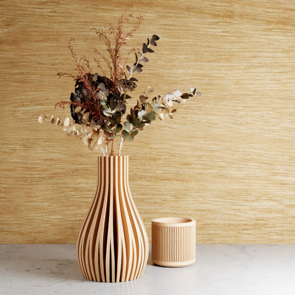 Wooden ribbed vase with vertical slats holding dried eucalyptus and grasses beside matching striped candle holder