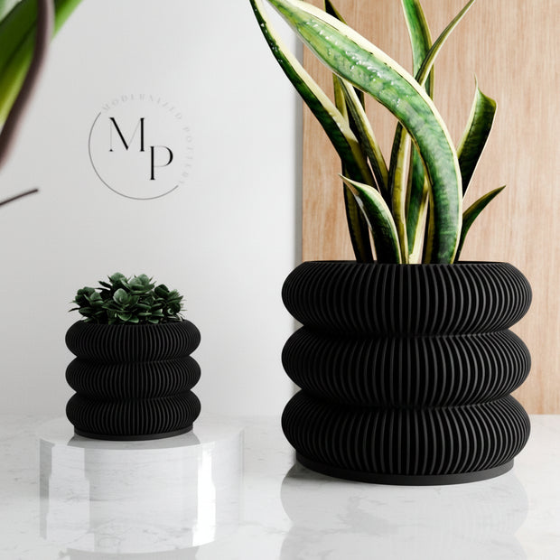 Ribbed wooden planters with stacked tiered rings holding snake plant and succulent on white marble surface with wood backdrop