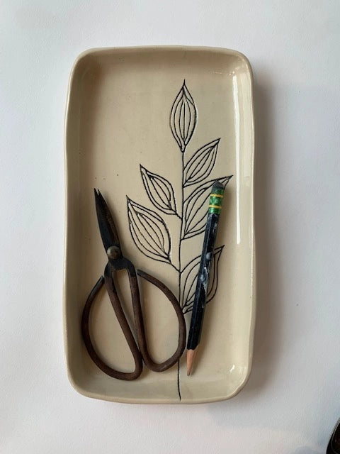 Cream ceramic rectangular catchall dish with black line drawing of botanical leaves holding small scissors and pen