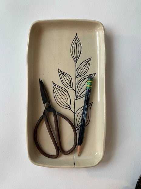Cream ceramic rectangular catchall dish with black line drawing of botanical leaves holding small scissors and pen