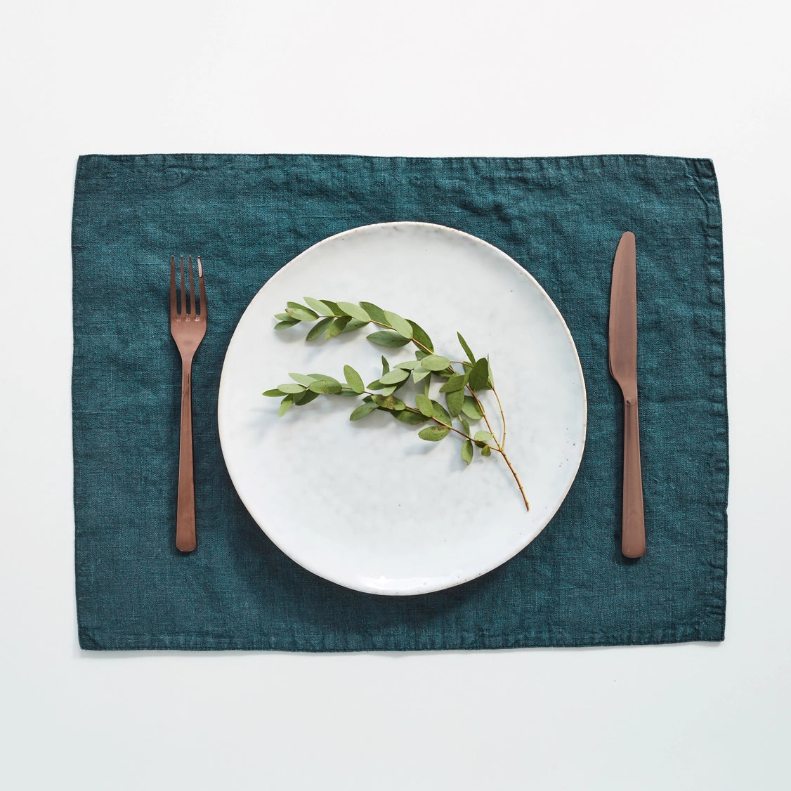 Teal blue linen placemat with textured weave, styled with white plate and copper flatware on neutral background