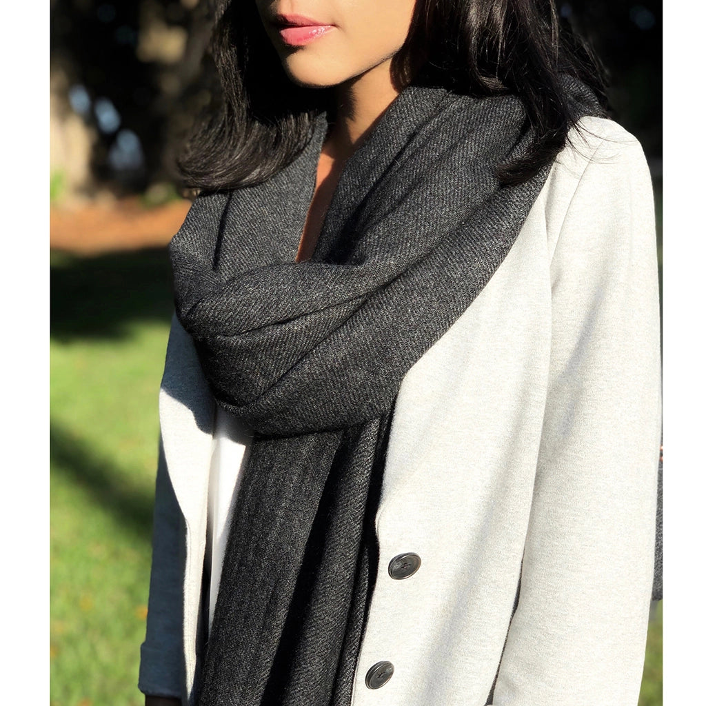 Charcoal gray textured cashmere scarf draped around neck, paired with cream wool coat, showing herringbone weave pattern