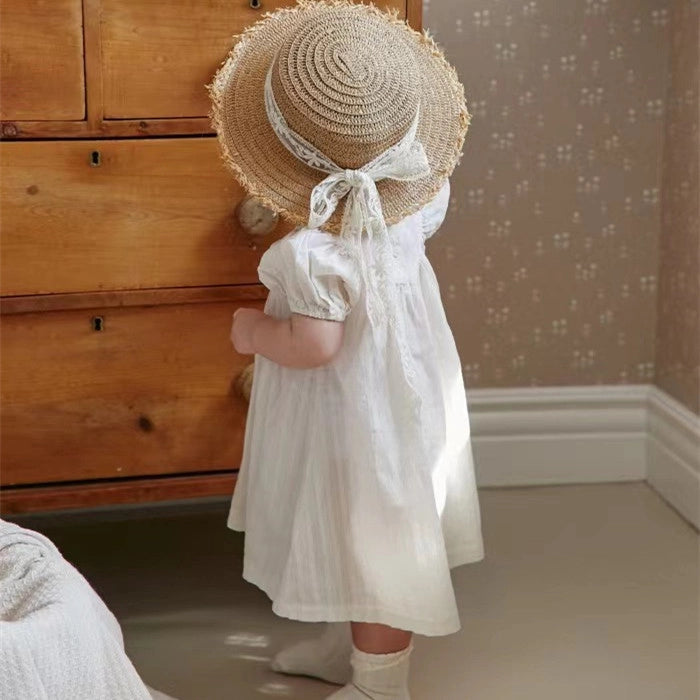 Natural straw sun hat with frayed edge and white ribbon tie paired with white cotton puff sleeve dress on child