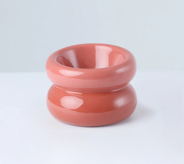 Stacked coral and terracotta glazed ceramic bowls with smooth rounded donut shape and glossy finish on white surface