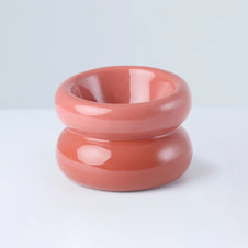 Stacked coral and terracotta glazed ceramic bowls with smooth rounded donut shape and glossy finish on white surface