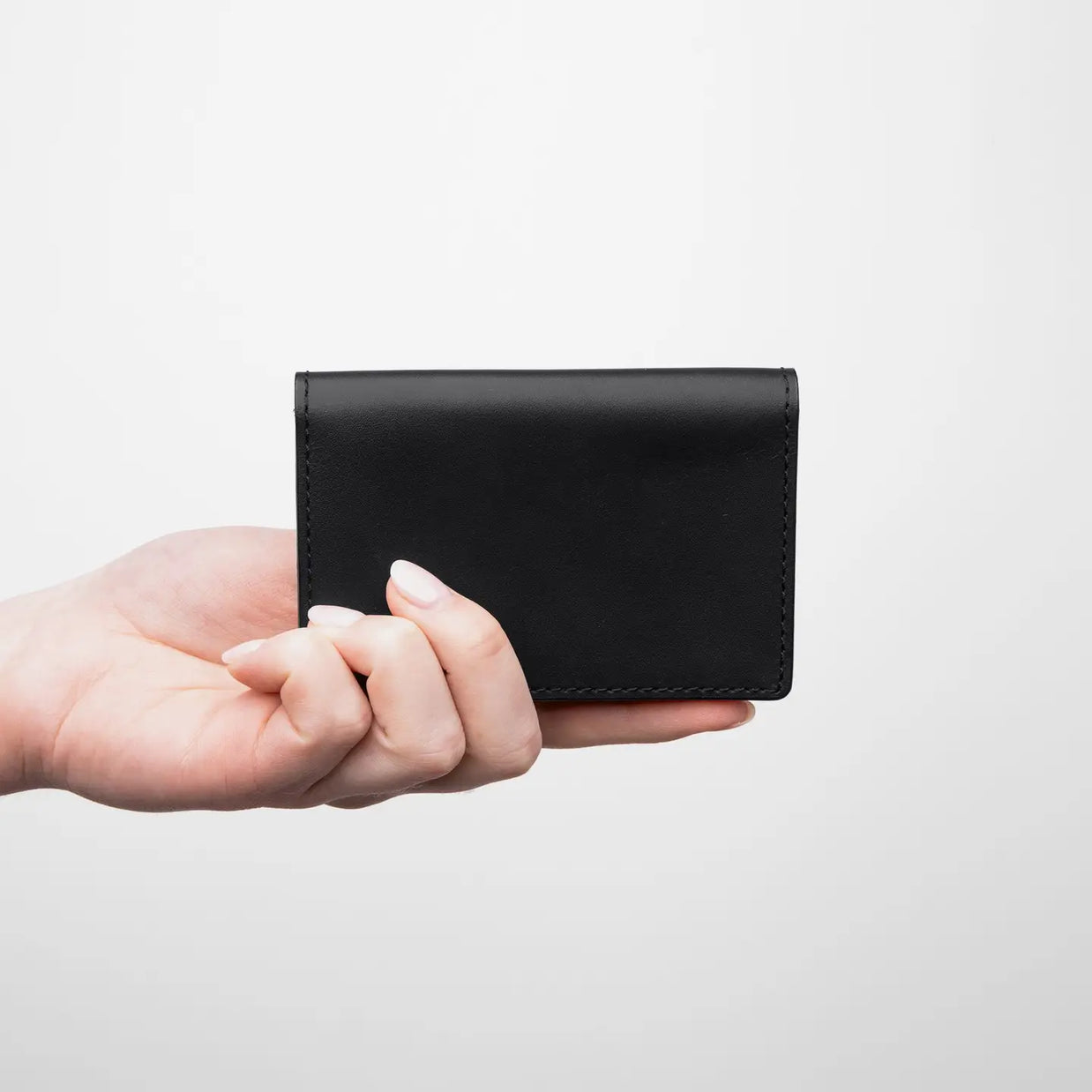 Black leather card holder wallet with visible stitching detail, held in hand showing compact size