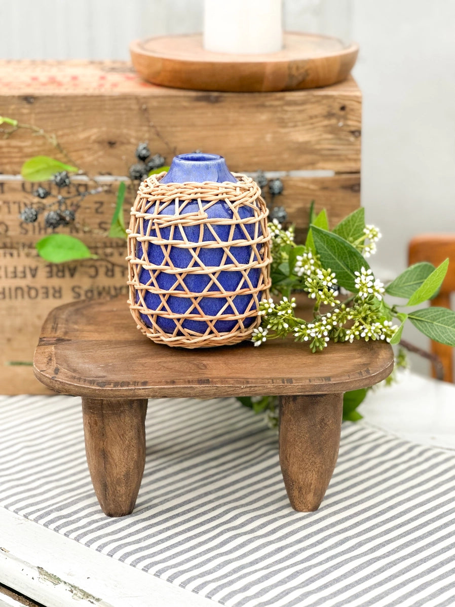 Cobalt blue ceramic vase wrapped in natural woven rattan basket cage with diamond lattice pattern on wooden stool
