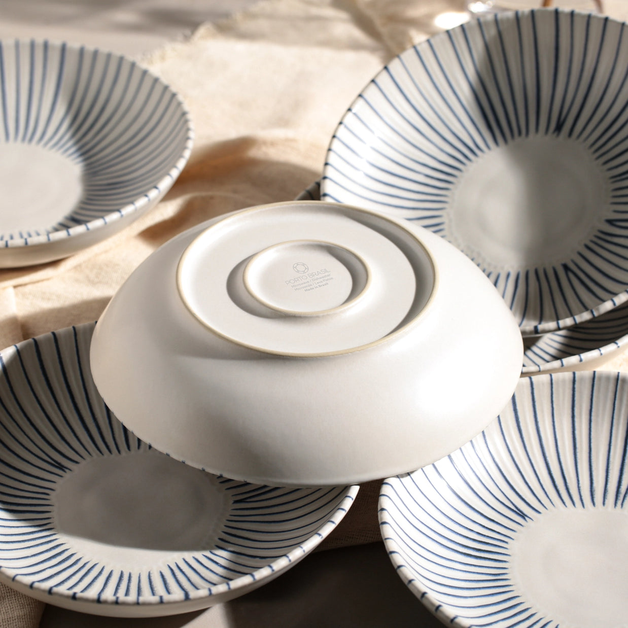 White ceramic bowls with navy blue radiating stripe pattern stacked artfully with natural linen napkin on neutral surface