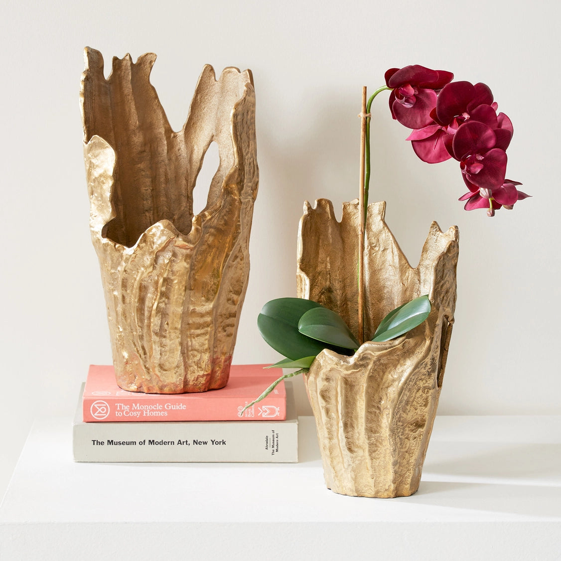 Two sculptural ceramic vases with irregular jagged rims in antique gold finish, one holding deep magenta orchid stems