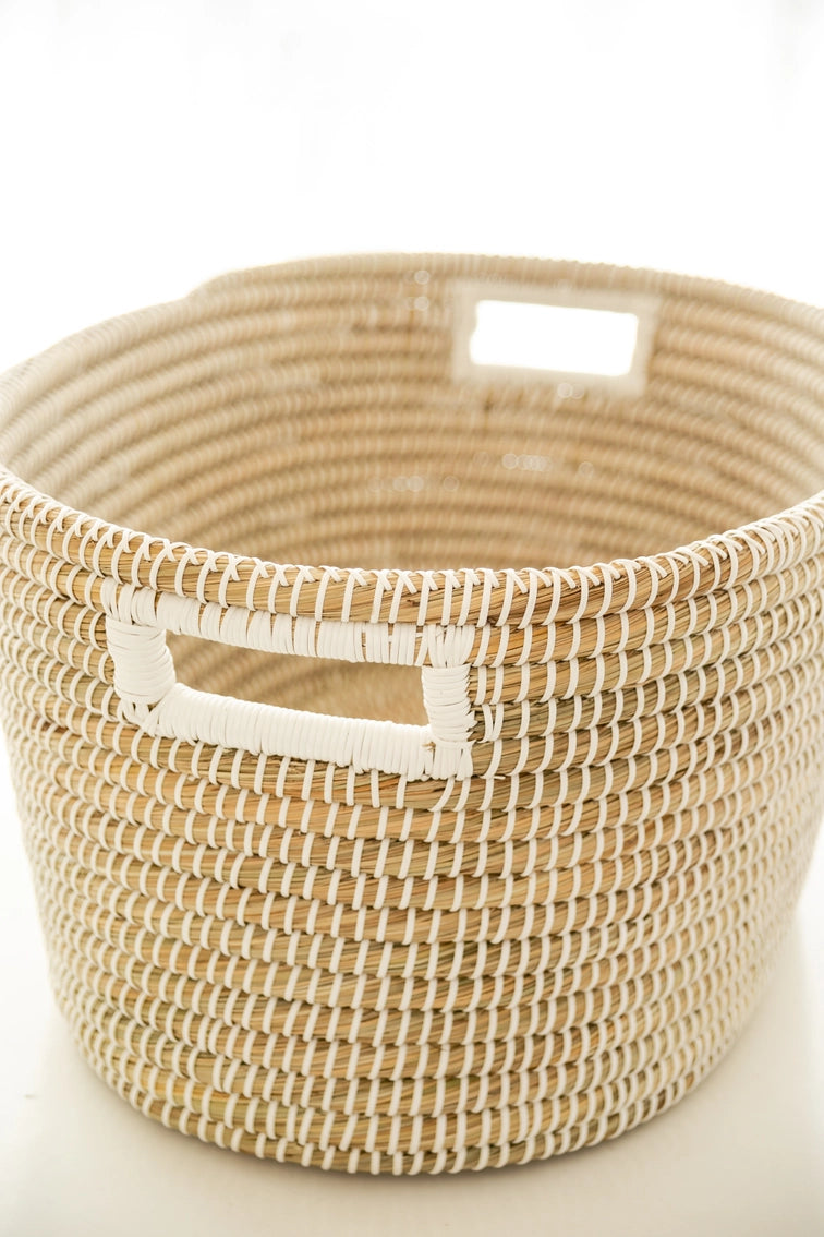 Round woven seagrass basket in natural tan and cream with tightly coiled pattern and rectangular cutout handles on sides