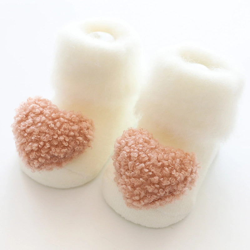 Cream fleece baby booties with dusty rose textured pom-poms on toes against white background