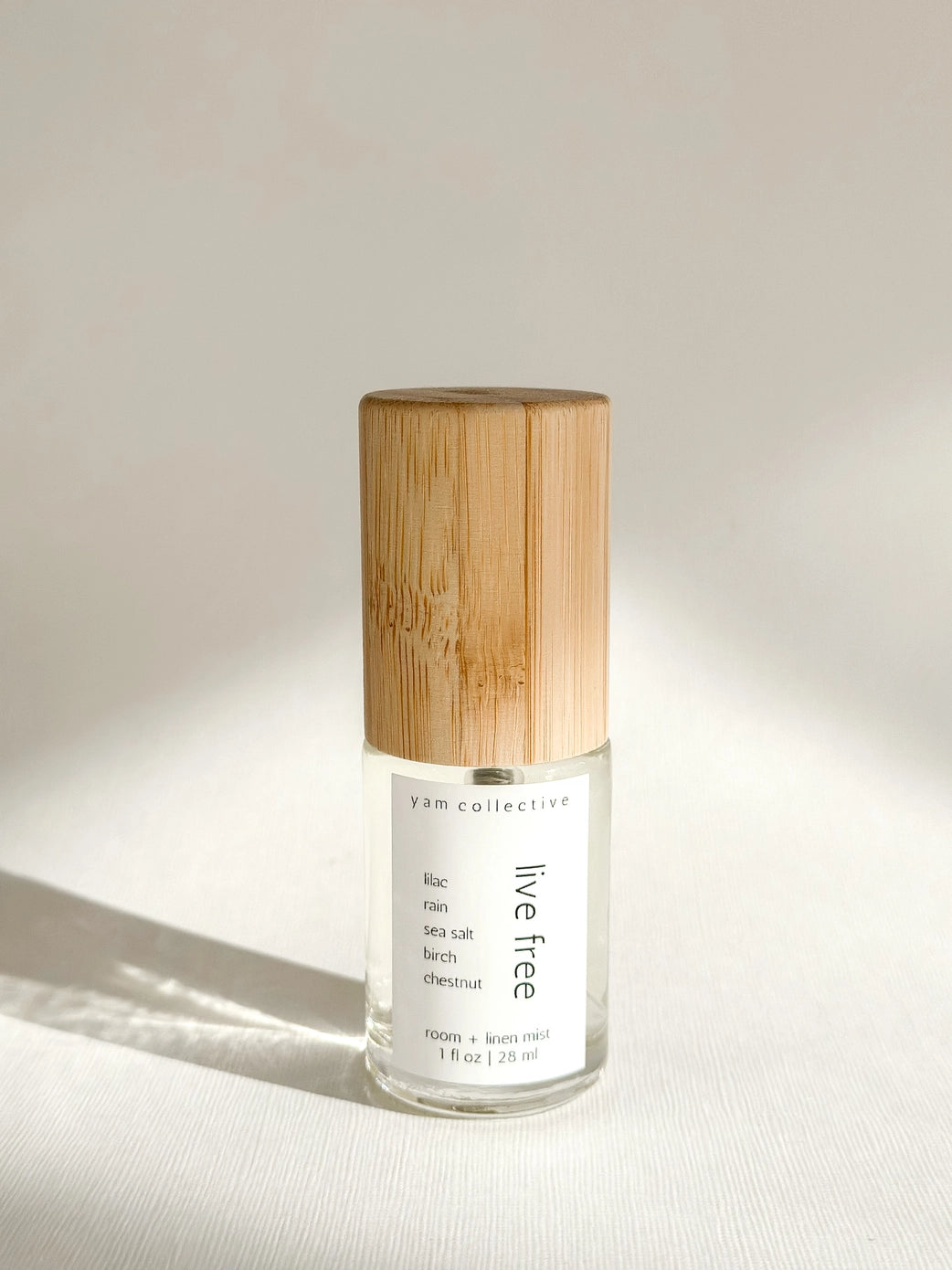 Clear glass room and linen mist spray bottle with natural wood grain bamboo cap labeled lilac free on white surface