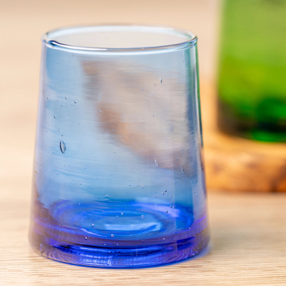Clear glass tumbler with gradient blue base, tapered cone shape, condensation droplets on smooth surface