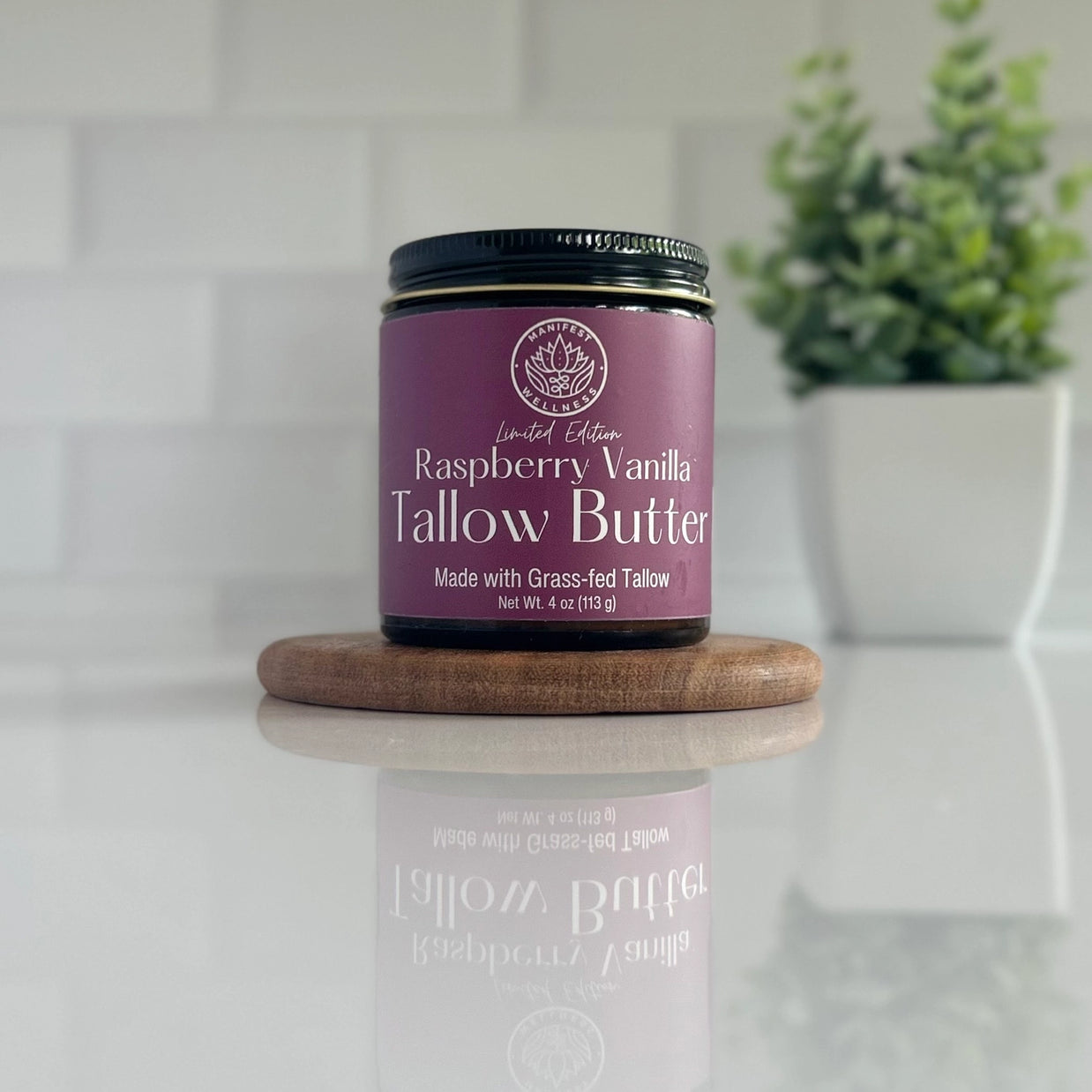 Container of Raspberry Vanilla Tallow Butter on a wooden coaster with a plant in the background.