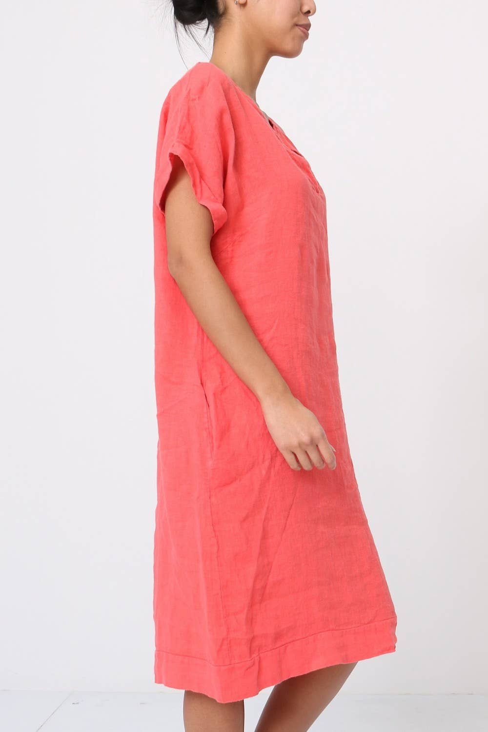Coral pink linen shift dress with relaxed fit, rolled short sleeves, and knee-length hem shown in side profile view