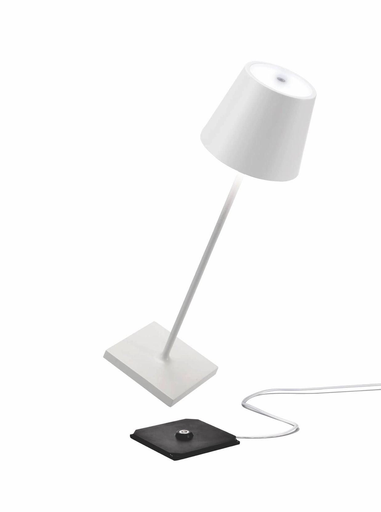 White cordless table lamp with tapered shade, angled stem, square base, and black wireless charging pad with cable