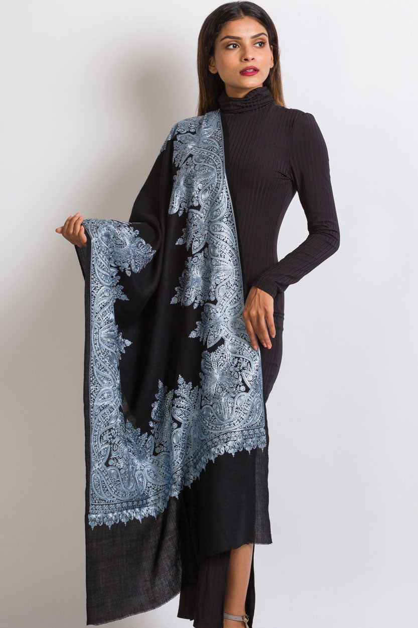 Black pashmina shawl with powder blue paisley embroidery border and frayed edges draped over ribbed turtleneck dress