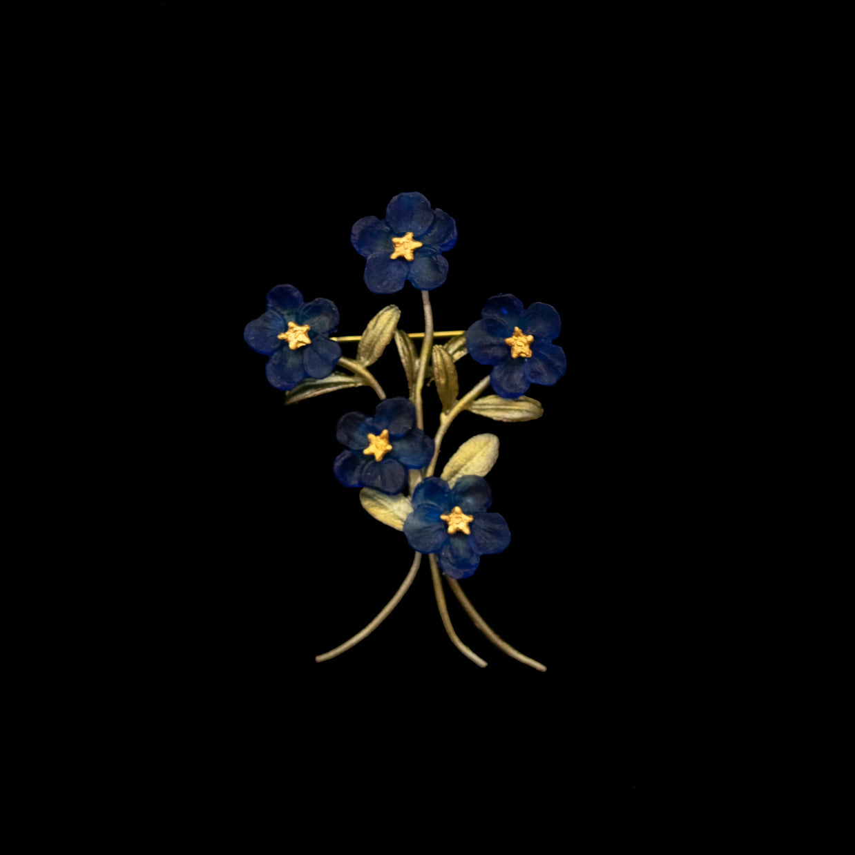 Gold-tone floral brooch with five deep blue violet flowers with yellow centers and textured leaves on curved stems