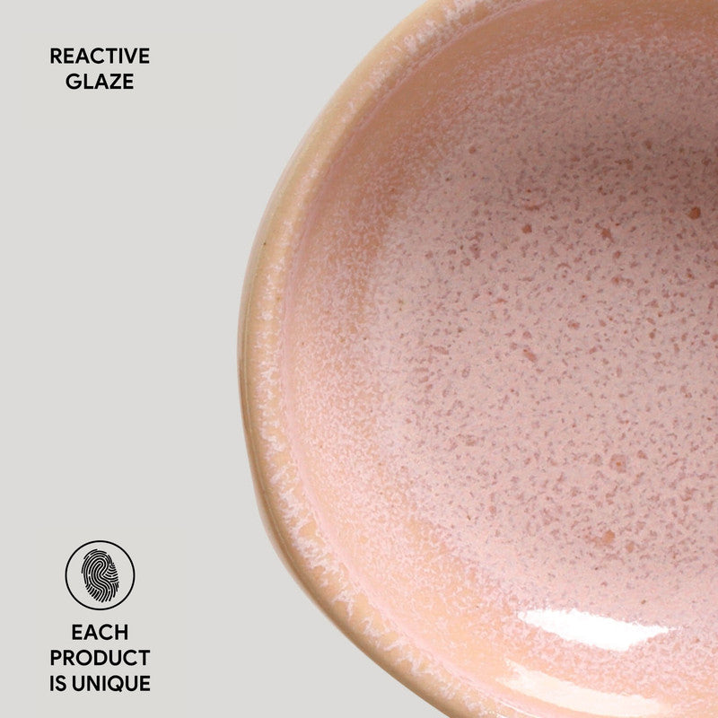 Handmade ceramic bowl in blush pink reactive glaze with speckled texture and cream-colored rim on beige background