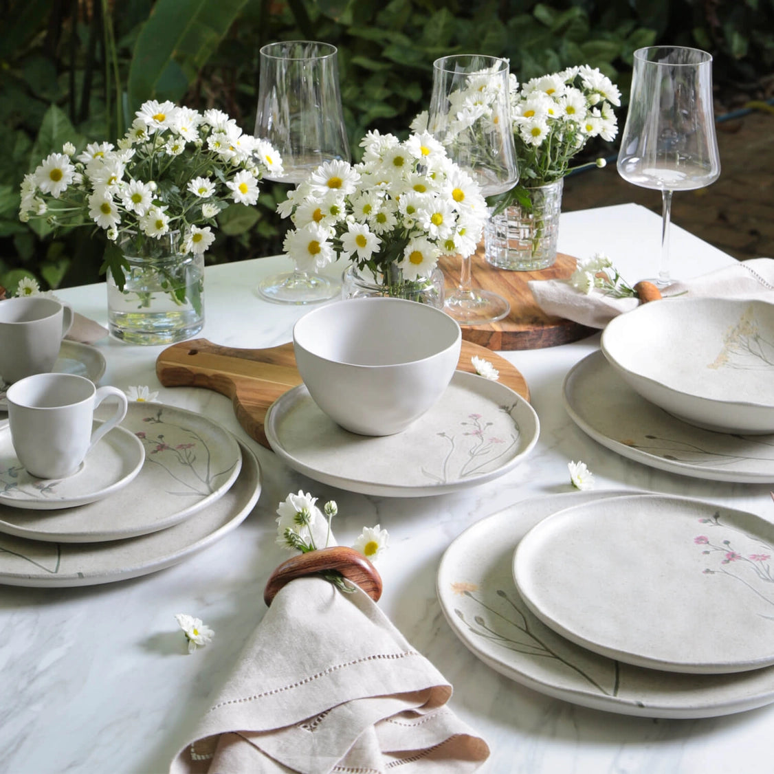 White ceramic soup bowl with delicate floral botanical pattern, displayed in outdoor table setting with daisies and glassware