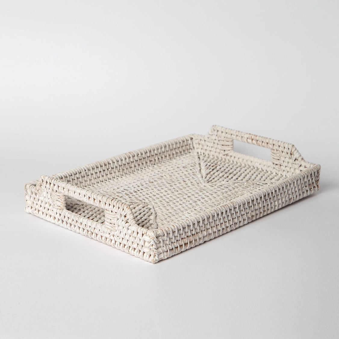Whitewashed rectangular rattan tray with woven texture, cut-out handles on sides, and shallow flat bottom for serving