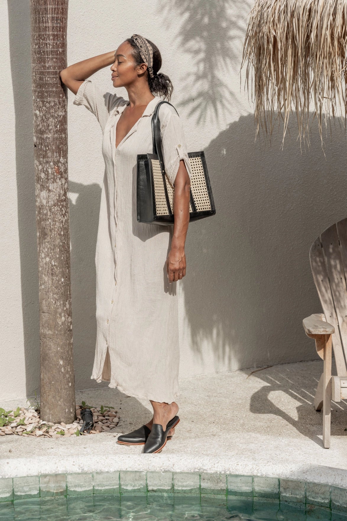 Black leather tote bag with natural rattan cane panels and top handles carried on shoulder by poolside