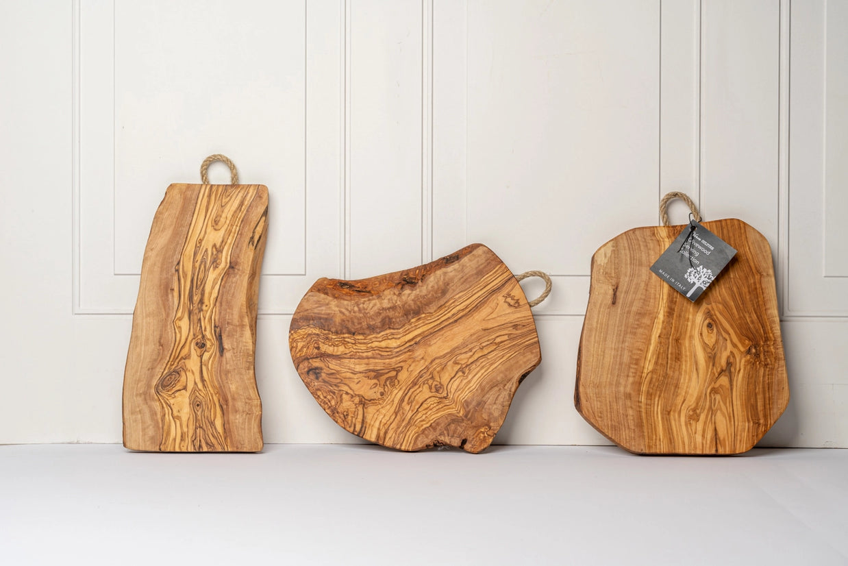 Three olive wood cutting boards with natural live edges, rope handles, and rich golden-brown grain patterns on white paneling
