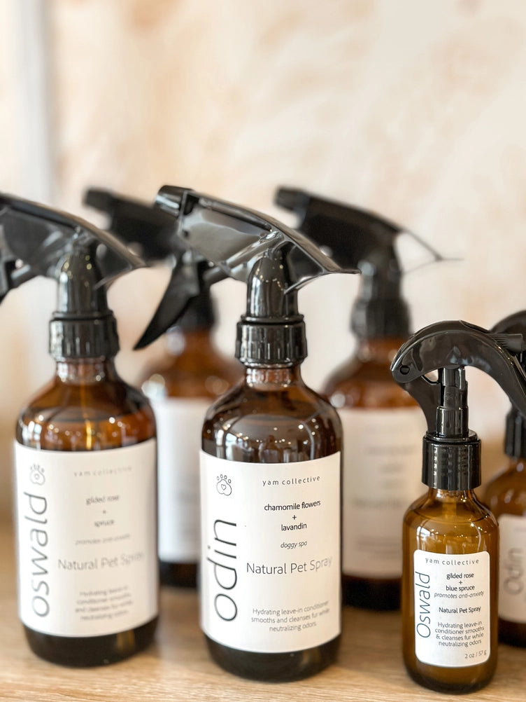 Amber glass spray bottles with black trigger nozzles and minimalist white labels displaying natural pet spray products