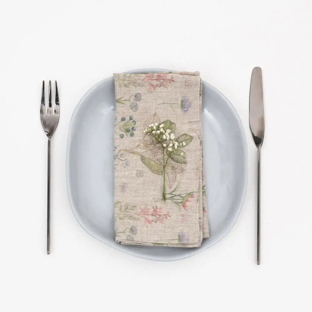 Natural linen napkin with vintage botanical floral print in soft pink, green, and blue hues, displayed on plate