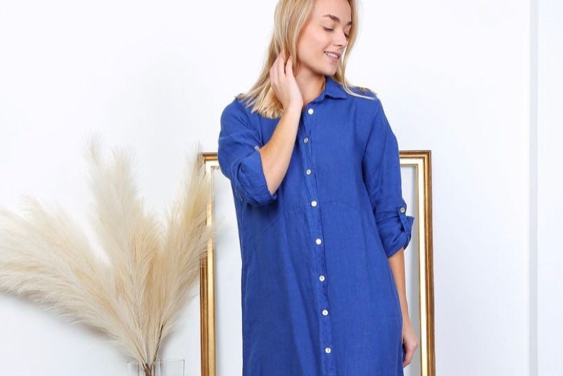 Cobalt blue linen shirt dress with white buttons, rolled sleeves, and relaxed A-line silhouette on blonde model