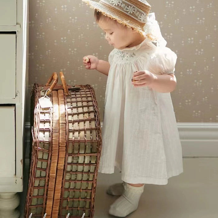White linen smocked dress with embroidered collar and puffed sleeves on toddler wearing straw boater hat with ribbon