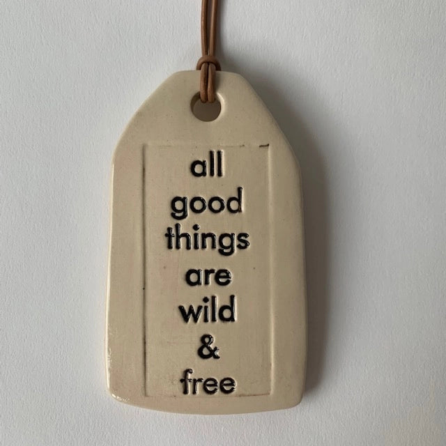 Cream ceramic tag with embossed text reading all good things are wild and free hanging from brown leather cord