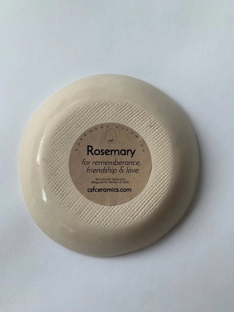 Bottom view of cream ceramic dish with ribbed texture and round kraft label reading Rosemary for remembrance friendship and love
